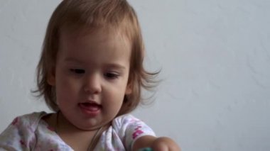 Güzel, sevimli, neşeli, gülümseyen, neşeli, enerjik, küçük, çıplak bir çocuk. Kıvırcık saçlı, uzun elbiseli bebek farklı duygular gösteriyor. Beyaz arka plan evde, yatakta.