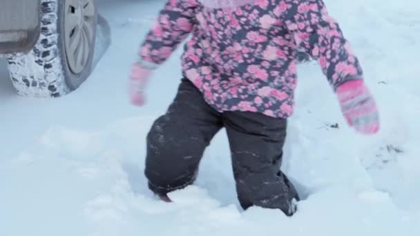 Inverno, vacanza, giochi, concetto di famiglia - slow-mo close-up bambino correre attraverso la neve profonda. i piedi dei bambini camminano su un sentiero innevato. bambino in età prescolare vestito di tuta nera in nevicata nella stagione fredda — Video Stock