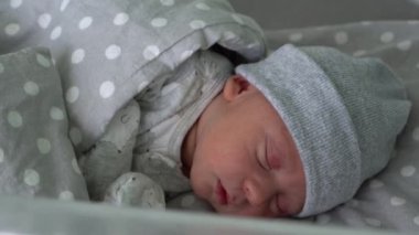 Yeni doğan bebek kırmızı şirin surat portresi. Eski günlerde gri arka planda, cam yatakta uyuyordu. Hayatın başlangıcındaki çocuk şapkayla. Bebekler, Doğum, Doğumun İlk Anları, Başlangıç Konsepti