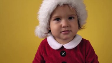 Duyguyu kapat. Mutlu, neşeli, tombul, bebek bebek Noel Baba kostümlü, sarı arka plandaki kameraya bakıyor. Çocuk Noel Sahnesi Oynuyor Doğum gününü kutluyor. Çocuk Yılbaşını Eğlenerek Geçiriyor