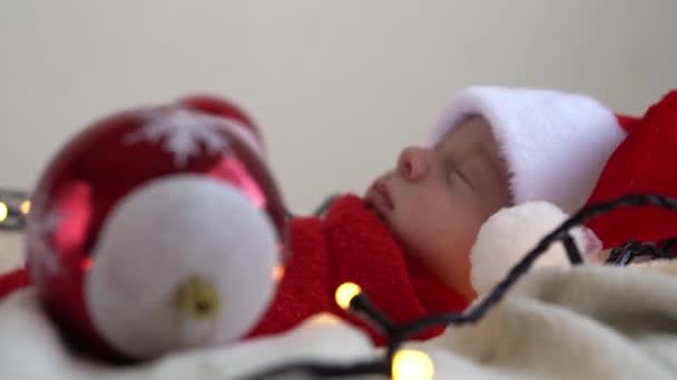 Close Up Retrato Primeiros Dias de Vida Recém-nascido Bonito Engraçado Adormecido Bebê Em Santa Chapéu Envolvido Em Fralda Vermelha Em Fundo Garland Branco. Feliz Natal, Feliz Ano Novo, Bebê, Infância, Conceito de Inverno — Vídeo de Stock