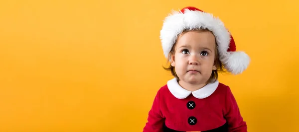Banner Portraite Happy Cheerful Chubby Baby Girl in Santa Suit Looking Up Interested At Yellow Background. Child Play Christmas Scene Celebrating Birthday. Kid Have Fun Spend New Year Time Copy Space Royalty Free Stock Images