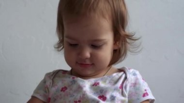 Güzel, sevimli, neşeli, gülümseyen, neşeli, enerjik, küçük, çıplak bir çocuk. Kıvırcık saçlı, uzun elbiseli bebek farklı duygular gösteriyor. Beyaz arka plan evde, yatakta.