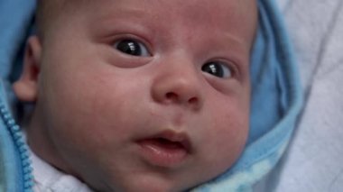 Kameradaki bebeğe bak. Yakın çekim. bebek, çocukluk, ebeveyn sevgisi, duygusal konsept - kahverengi gözlü tombul bebeğin sevimli gülen yüzü yumuşak mavi ceketli bebek uyanık yatağında yatıp etrafına bakıyor