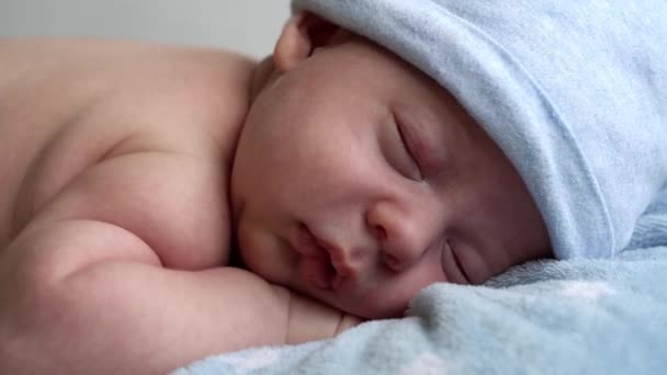 Kojence, dětství, vývoj, zdraví, láska, péče koncept - pohled shora zblízka tvář novorozence nahé spací malý kojenec chlapeček v klobouku ležící na břiše na měkké modré banket na posteli doma — Stock video