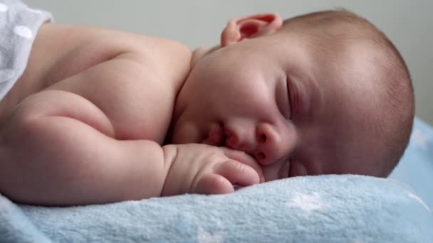 Kojence, dětství, vývoj, medicína a zdraví, láska, péče koncept - close-up tvář novorozence nahé spací malý kojenec chlapec ležící na břiše na měkké modré banket na posteli doma — Stock video