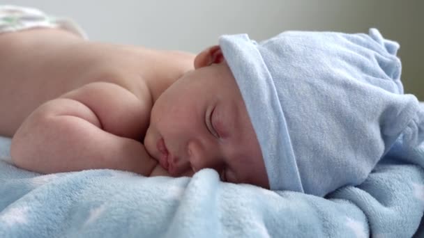 Kojence, dětství, vývoj, zdraví, láska, péče koncept - pohled shora zblízka tvář novorozence nahé spací malý kojenec chlapeček v klobouku ležící na břiše na měkké modré banket na posteli doma — Stock video