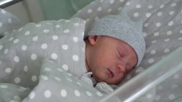 Recém-nascido bebê vermelho bonito rosto retrato primeiros dias dormindo na cama de vidro médica em fundo cinza. Criança no início minutos de vida no chapéu. Bebês, Parto, Primeiros Momentos de Borning, Princípio de Início — Vídeo de Stock