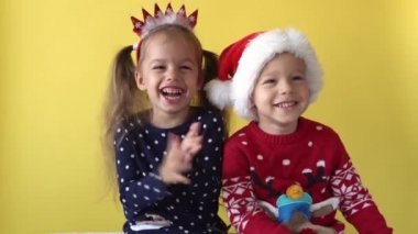 Duygusal Sevimli Mutlu Neşeli İki Kardeş Arkadaş Bebek Kız ve Noel Baba Takım Elbiseli Çocuk sarı arka planda kameraya bakıyor. Doğum gününü kutlayan çocuk Noel Sahnesi oynuyor. Çocuk Yılbaşını Eğlenerek Geçiriyor