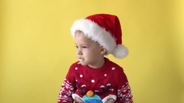 Retrato emoción lindo feliz alegre regordete preescolar bebé sonriendo tonteando alrededor en santa hat buscando en cámara en amarillo fondo. Celebración de Navidad infantil. El niño se divierte pasar el tiempo de año nuevo — Vídeos de Stock