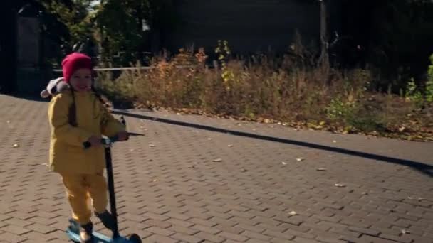 Poco lindo preescolar menor bebé hermanos niña y niño montar scooter rápidamente, jugar juego de destilación tienen raza hojas caídas amarillas mirar a la cámara clima frío en Fall Park. Infancia, Familia, Otoño — Vídeo de stock