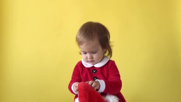 Πορτραίτο συναίσθημα χαριτωμένο χαμογελώντας ευτυχισμένη χαρούμενη μωρό κοριτσάκι σε κοστούμι Σάντα κοιτάζοντας κάμερα στο κίτρινο φόντο. Παιδί Παίξτε Χριστουγεννιάτικη Σκηνή Γιορτάζοντας Γενέθλια. Καλά να περάσετε την Πρωτοχρονιά — Αρχείο Βίντεο