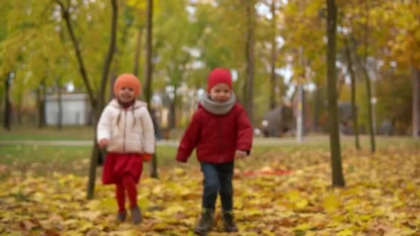 Two happy funny active smilling friends children kids boy Girl walking running holding hands in park forest enjoying autumn fall nature weather. Kid in red cloth playing hiding behind trees Slow — Stock Video