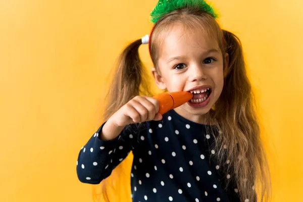 Retrato positivo alegre sorrindo feliz colegial menina árvore de Natal decoração polka dot dress biting comer cenouras laranja no fundo laranja. Ano Novo, férias, celebração, conceito de inverno Imagens Royalty-Free