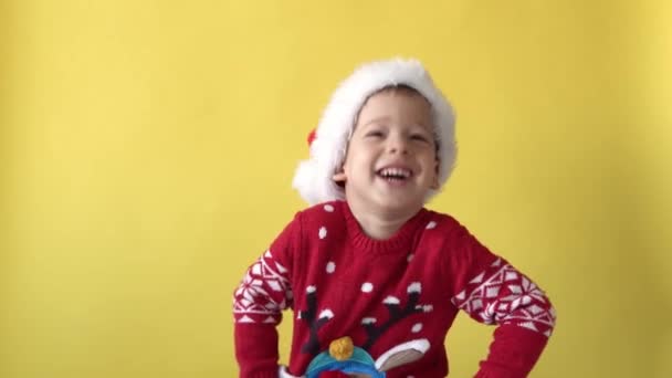 Πορτρέτο Συναίσθημα Χαριτωμένο Χαρούμενο Χαρούμενο Τσάμπι Νηπιαγωγείο Αγόρι Γελάει Γελώντας Γύρω Στο Σάντα Χατ Κοιτάζοντας Κάμερα Σε Κίτρινο Φόντο. Παιδικά Χριστούγεννα Γιορτάστε. Καλά να περάσετε την Πρωτοχρονιά — Αρχείο Βίντεο