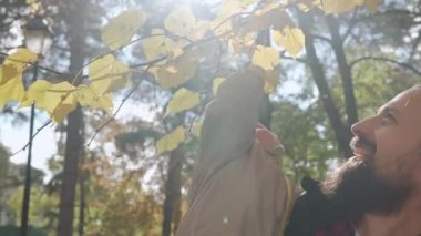 Genç baba sakalı küçük mutlu bebek kucağında. Kucağında sarı yapraklar var. Güneşli bir günde, Soğuk Hava Ormanı Parkı 'nda. Baba kızıyla yürüyor, çocukluk, aile...