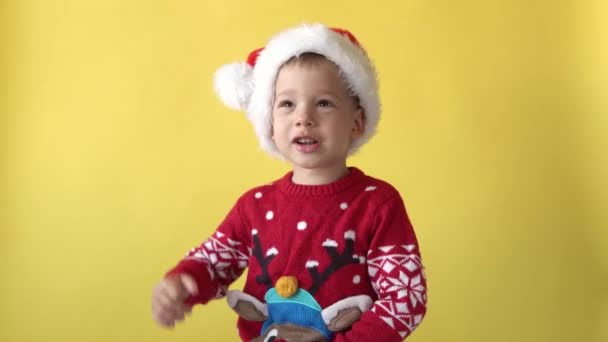 Retrato Emoção bonito feliz alegre gordinha pré-escolar bebê menino sorrindo brincando em Santa Hat Looking On Camera At Yellow Background. Celebração do Natal Infantil. Criança Divirta-se Passe o Ano Novo — Vídeo de Stock