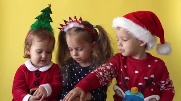 Emotie schattig gelukkig 3 vrienden meisje jongen putting hand samen in Santa pak op zoek naar camera op gele achtergrond. Kind Spelen Kerst Scene vieren verjaardag. Kind veel plezier besteden Nieuwjaar tijd — Stockvideo