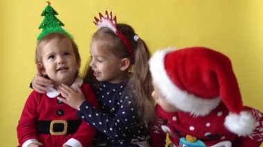 Duygusal Sevimli Mutlu Neşeli 3 Kardeşler Arkadaşı Bebek Oğlan, Noel Baba Takım Elbisesi içinde sarılıp Sarı Arkaplan 'daki kameraya bakıyor. Doğum gününü kutlayan çocuk Noel Sahnesi oynuyor. Çocuk Yılbaşını Eğlenerek Geçiriyor