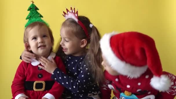 Emoción linda feliz alegre 3 hermanos amigos bebé niña abrazo en traje de Santa mirando en la cámara en el fondo amarillo. Niño Juega Escena de Navidad Celebrando el Cumpleaños. El niño se divierte pasar el tiempo de año nuevo — Vídeos de Stock