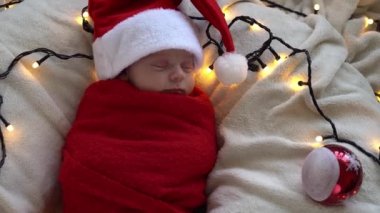 Yeni doğan bebeğin ilk portresi beyaz çelenk arka planında kırmızı beze sarılı, Noel Baba şapkalı komik uyuyan bebek. Mutlu Noeller, Mutlu yıllar, Bebek, Çocukluk, Kış Konsepti