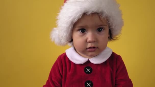 Detailní emoce Roztomilý šťastný veselý buclatý batole dítě dívka v santa oblek při pohledu na kameru na žlutém pozadí. Dítě hraje vánoční scénu slaví narozeniny. Dítě bavte se strávit Nový rok — Stock video