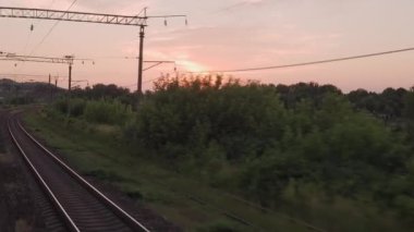 Pencereden yüksek hızlı tren manzarası güzel doğa manzarası vahşi arazi ve orman rayları yaz arkaplanında akşam günbatımında tren rayları. Ulaşım, seyahat, demiryolu, iletişim konsepti