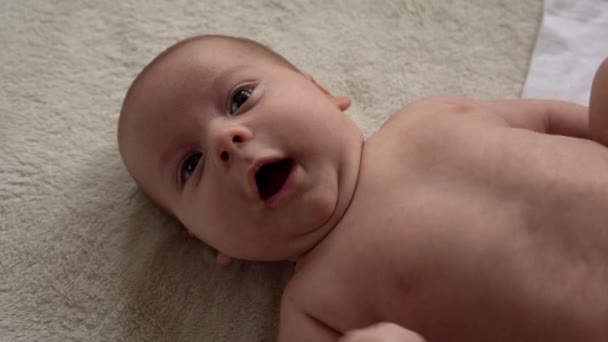 Jeugd, moederschap, familie, hygiëne, baby concept Close-up Gelukkige speelse nake kid 2 maanden pasgeboren jongen kijkend naar camera na bad douche op wit zacht bed. baby kind wakker tijd voor het slapen gaan — Stockvideo