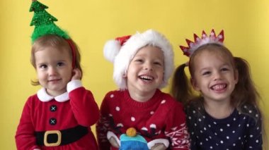 Sevimli, mutlu, neşeli, 3 kardeş arkadaş, bebek kız ve Noel Baba kılığındaki çocuk, sarı arka plandaki kameraya bakıp gülümsüyor. Çocuklar Noel 'i kutluyor. Çocuk Yılbaşını Eğlenerek Geçiriyor