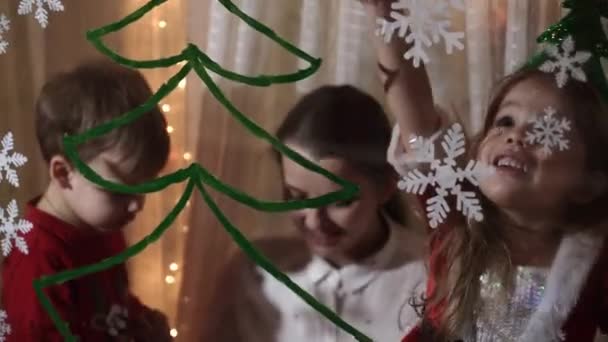 Otantik sevimli bir anne ve iki küçük anaokulu öğrencisi kız ve erkek kardeş 2-4 yaşlarında pencereye Noel ağacı çiziyor. Çocuklu genç bir kadın kar taneleri yapıştırıyor. Xmas, yeni yıl, kış konsepti. — Stok video