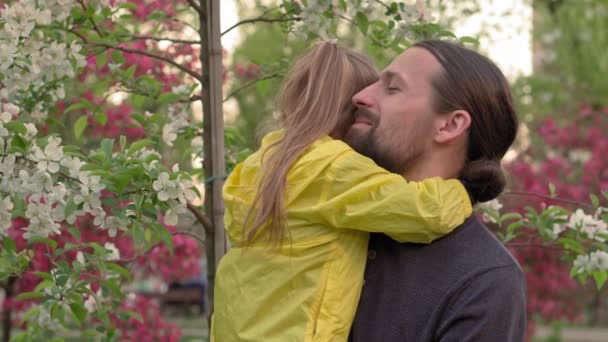 People in park. dad hold baby daughter girl in arms near blossoming apple tree and sniffing flowers. parents and fun children walking outdoors in open air. Fathers day, childhood, parenthood concept — Stock Video