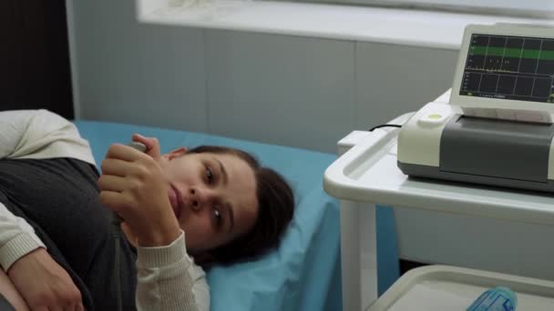 Mladá těhotná žena na nemocničním gauči během lékařské kontroly kardiotokografie. Navštivte gynekologa Doktor na klinice pro těhotenské poradce. Prozkoumat očekávaný břicho dítě matka zdravotní péče check up — Stock video