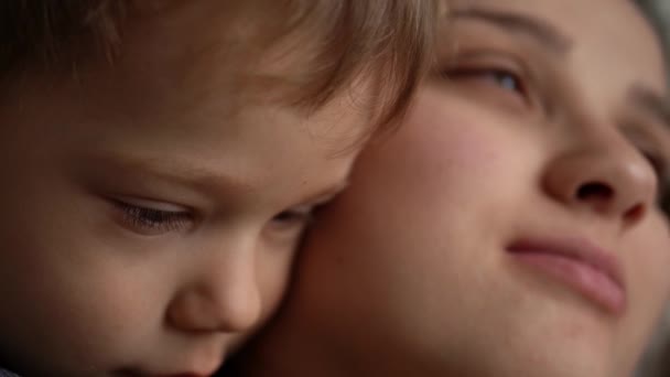 Маленьке миле сонне маля, ніжно обійняте поцілунком і піклуючись, розслабиться і обійме маму, яка посміхається. Дитинство, материнство, концепція любові. Діти емоцій. Малюк зосереджений на погляді. Портрет Кавказького хлопчика — стокове відео