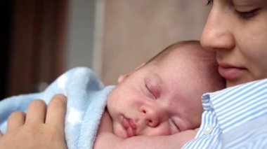 annelik, çocukluk, aile, bakım, sağlık, annelik konsepti - sıcak mavi battaniyeye sarılı yeni doğmuş bebek anne göğsünün kollarında uyuyor. Anne rahatla, kucağında öpücükle kucağında bebekle evde.