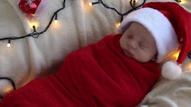Yeni doğan bebeğin ilk portresi beyaz çelenk arka planında kırmızı beze sarılı, Noel Baba şapkalı komik uyuyan bebek. Mutlu Noeller, Mutlu yıllar, Bebek, Çocukluk, Kış Konsepti