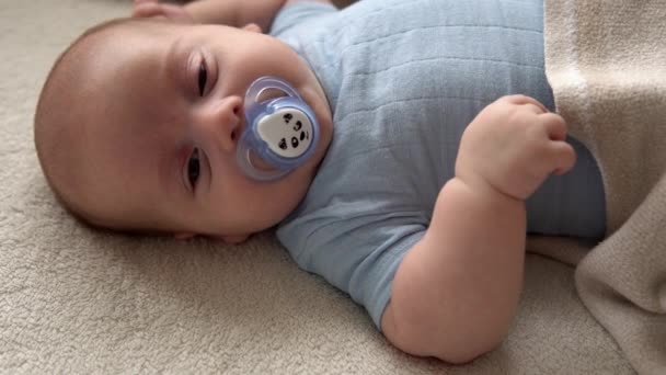 Close-up drăguț amuzant copil 2 luni nou-născut băiat cu suzetă uita-te la camera după duș baie pe pat moale alb. Copilul se trezește înainte de culcare. Copilărie, Maternitate, Familie, Concept pentru sugari — Videoclip de stoc
