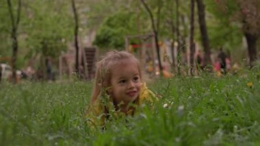 Sarı elbiseli, otantik, şirin bir anaokulu çocuğu bahar günbatımında çimlerde sürünen çiçekler topluyor. Güneş doğarken doğadaki çocuk. Çocukluk, ebeveynlik, aile, yaşam tarzı konsepti