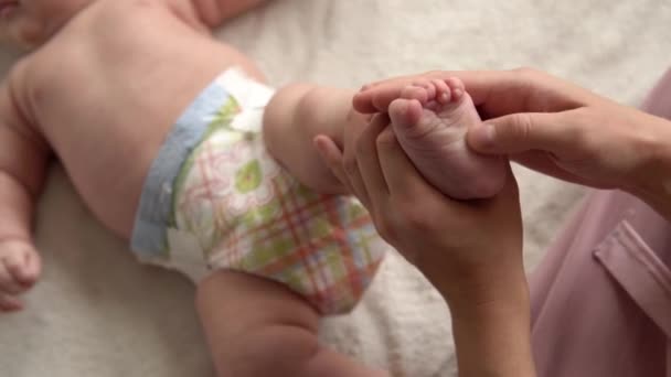 Salute la cura della pelle, pediatria di sviluppo, le mani della madre del primo piano del bambino danno nudo neonato massaggio bambino su braccia, gambe, dita, riflesso sui piedi esercizio, sfregamento petto addome pelle sul letto a casa — Video Stock