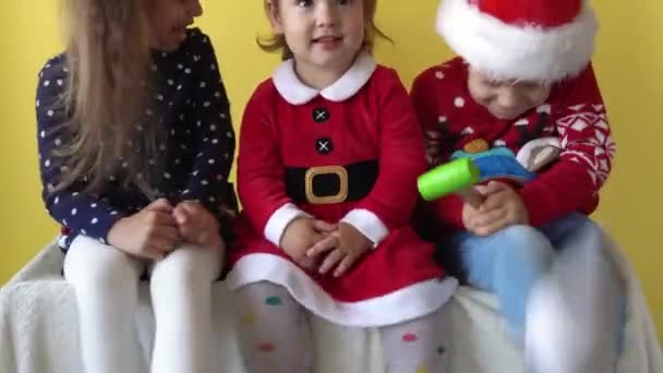 Emotion Cute Happy 3 Siblings Friend Baby Girl And Boy Wave Feet In Santa Suit Looking On Camera At Yellow Background. Child Play Christmas Scene Celebrating Birthday. Kid Have Fun Spend New Year Time — Stock Video