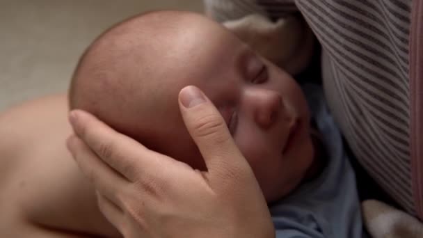 Μητρότητα, παιδική ηλικία, οικογένεια, φροντίδα, υγεία, μητρότητα - κλείστε τον ύπνο νεογέννητο σε μπλε κοστούμι του σώματος κοιμάται σε χέρια χέρι μητέρα στήθος. Μαμά εγκεφαλικά επεισόδια πρόσωπο φιλί αγκαλιά κρατώντας το μωρό μωρό στο κρεβάτι στο σπίτι — Αρχείο Βίντεο