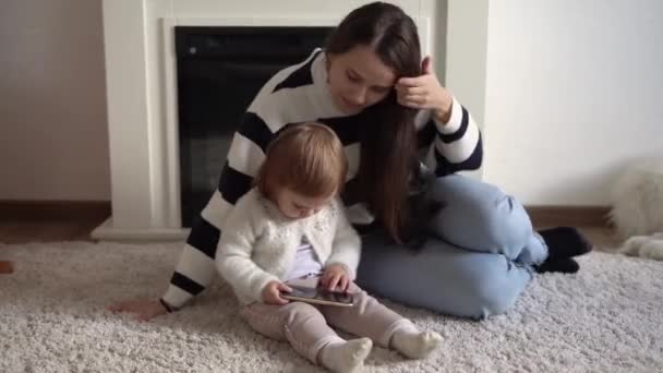 Glada bedårande småbarn dotter njuta av att lära sig att använda smart telefon med föräldrakontroll. Lycklig familj ung förälder mamma visar roliga tecknade mobilapp, titta på videor avkopplande hemma — Stockvideo