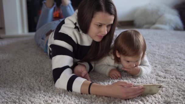 Glada bedårande småbarn dotter njuta av att lära sig att använda smart telefon med föräldrakontroll. Lycklig familj ung förälder mamma visar roliga tecknade mobilapp, titta på videor avkopplande hemma — Stockvideo