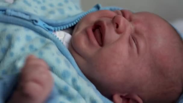 Sguardo del bambino in macchina fotografica primo piano girato. bambino, infanzia, amore dei genitori, concetto di emozione - piangendo viso affamato di paffuto dagli occhi marroni neonato in morbida giacca blu grido sveglio sdraiato sul letto a casa — Video Stock