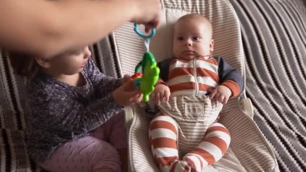 Infância, maternidade, família, conforto. Menino recém-nascido em pijama de macacão listrado acordado olhando ao redor sorri brinca com chocalhos irmã reconhece mãe no quarto em casa atmosfera — Vídeo de Stock