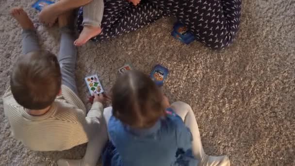 Childhood, education, hobby, family, friends, friendship concept. Happy young mother mum babysitter with little preschool kids children spend time playing card game on floor at home by fireplace — Stock Video