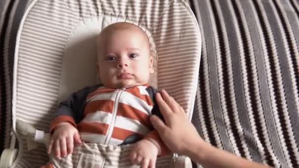 Kijk van baby in camera close-up zuigeling, jeugd, ouderlijke liefde. Schattig lachend gezicht pasgeboren in gestreepte bodysuit pyjama wakker kijk rond liggend op zachte stoel thuis. vreugdevolle levensstijl van gelukkig kind — Stockvideo