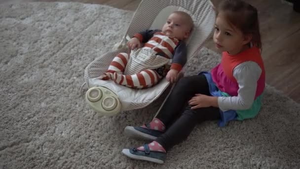 Enfance, maternité, famille, confort. Petit nouveau-né garçon en pyjama à rayures costume de corps éveillé regardant autour de sourires joue hochets frère soeur enfant lul amusant frère dans la chambre à la maison atmosphère — Video