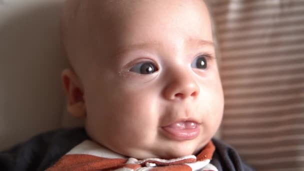 Mirada de bebé en cámara de cerca bebé, infancia, amor de los padres. Linda cara sonriente recién nacido en pijama de traje de cuerpo rayado mirada despierta alrededor de la colocación en la silla suave en casa. estilo de vida alegre de niño feliz — Vídeo de stock