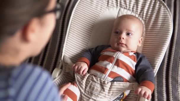 Sobre o ombro face a face segurar Infância, maternidade, família. Menino recém-nascido em pijama de macacão listrado acordada olha ao redor sorrindo toca chocalhos reconhece mãe em casa atmosfera — Vídeo de Stock