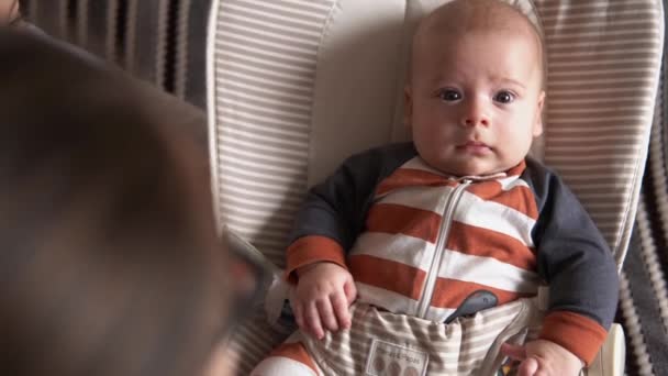 Sobre el hombro cara a cara mantenga la infancia, la maternidad, la familia. pequeño bebé recién nacido chico en rayas cuerpo pijama despierto mira alrededor sonriendo obras de teatro sonajeros reconoce mamá en el hogar atmósfera — Vídeo de stock